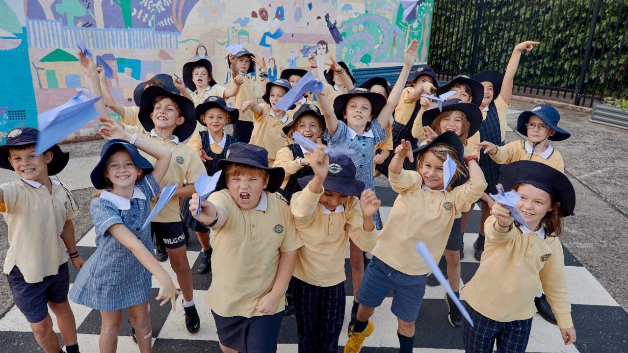 Agroup of school students smiling and flying paper planes in a school playground.